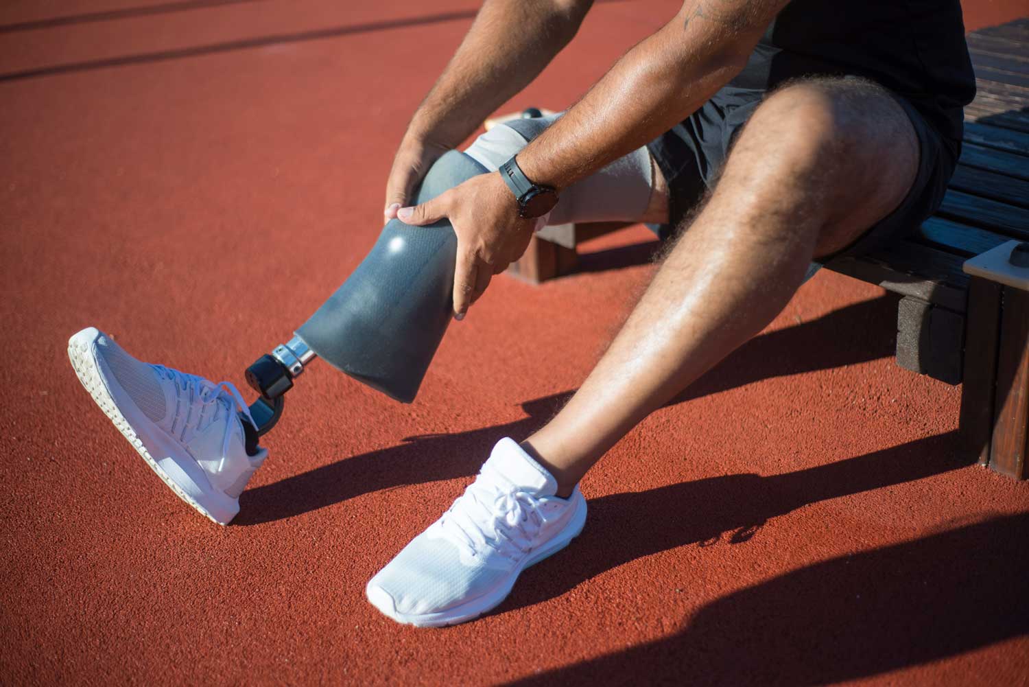 Man at a track putting sleeve over prosthetic leg before exercising